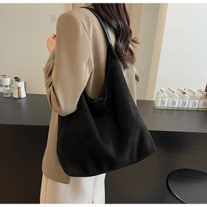 Close-up of large black suede tote bag with minimalist shoulder strap on female model