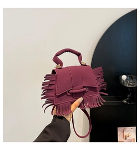 Détail d'un sac bandoulière bordeaux avec franges à glands et fermoir métallique