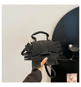 Détail d'un sac carré noir avec de longues franges et une large poignée supérieure