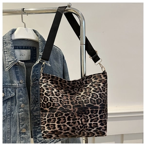 Detail of leopard print tote bag featuring a black wide strap and golden metal buckles