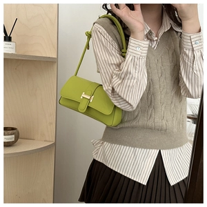 Detail of green leather baguette bag with gold H buckle worn as an underarm shoulder bag