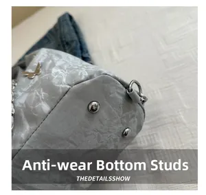 Détail du logo papillon et des clous de fond en métal sur le sac seau gris nuage