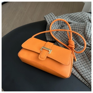 Close-up of orange baguette bag with gold buckle and knotted shoulder strap detail