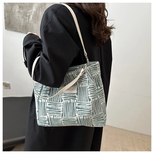 Detail of a green and white striped canvas tote bag with slim white leather shoulder straps