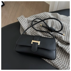 Detailed top view of black leather baguette bag with gold metal clasp and knotted strap