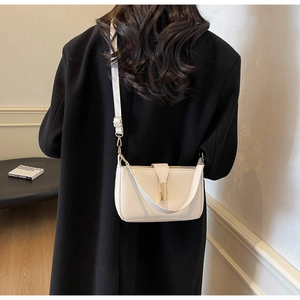 Detail of cream leather crossbody bag with gold buckle on model in black coat
