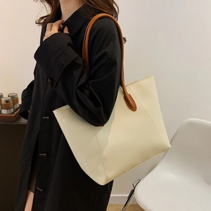 Minimalist large capacity cream leather tote bag with brown straps worn by a model