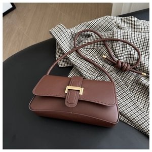 Top view of a brown leather baguette bag with gold buckle on a black textured surface