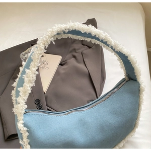 Détail d'un sac hobo en denim bleu avec bordure en peau de mouton blanche et fermeture éclair