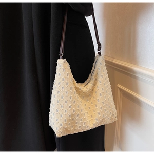Detail of cream woven tote bag with fringe texture and leather strap worn by a model