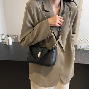 Minimalist black leather crossbody square bag with gold buckle on a model shoulder