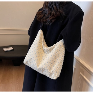 Detail of stylish cream tote bag with blue cross pattern worn over a black coat