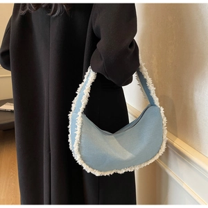 Détail du sac hobo en jean bleu clair avec bords effilochés sur manteau noir