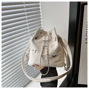 Détail du sac seau en cuir blanc avec charms papillon argentés et cordon en chaîne