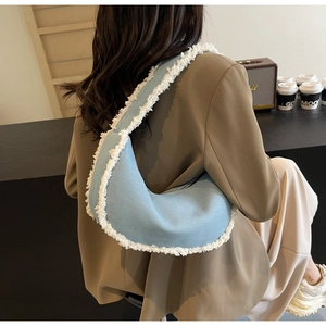 Sac hobo en denim bleu avec franges blanches porté par un mannequin dans un café chic