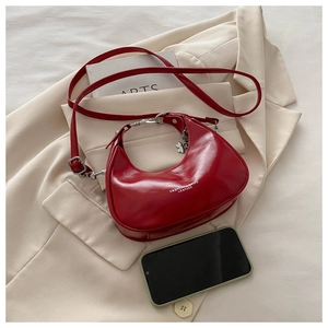 Detail of red crescent shoulder bag with heart pendant on a beige blazer