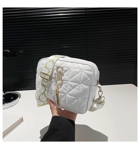 Detailed view of white quilted bag with golden S logo tassel and patterned wide strap