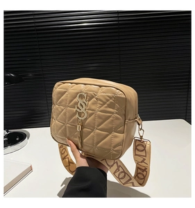 Detail of quilted beige crossbody bag with gold S-logo, tassel, and jacquard strap