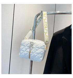 Close-up of white quilted crossbody bag with golden tassel and patterned wide strap