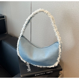 Détail du sac croissant en denim bleu clair avec bordure à franges blanches et zip argent
