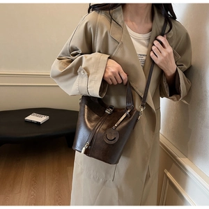 Détail du sac seau rétro en cuir marron avec fermeture éclair et pendentif smiley