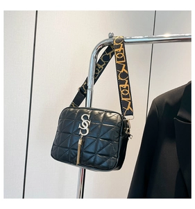 Detail of black quilted crossbody bag with golden S-logo and fringe tassel charm