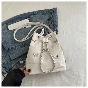 Détail du sac seau blanc avec texture ondulée et décoration papillon en métal argenté