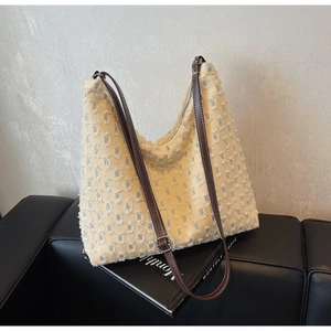 Detail of beige tweed hobo bag with adjustable brown leather strap on a black leather sofa
