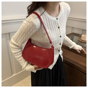 Detail of red glossy hobo bag with gold buckle on shoulder of model in white knitwear