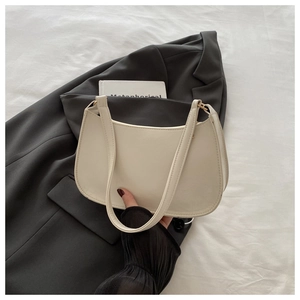 Detail of minimalist ivory half-moon shoulder bag held against a chic fashion backdrop
