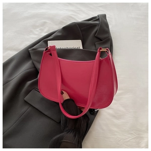 Close-up of a glossy rose red hobo shoulder bag with golden hardware on a grey blazer