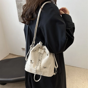 Sac seau blanc avec breloques papillon argentées et chaîne sur un manteau noir