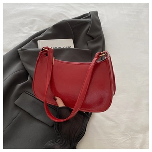 Detail of red patent leather underarm bag with sleek crescent shape and gold hardware