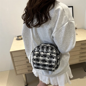 Checkered heart print shoulder bag with woven strap shown on model in a cozy interior