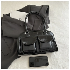 Detail of black glossy handbag with dual pockets on gray blazer in minimalist setting