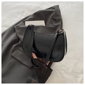 Detail of black glossy hobo bag featuring a gold ring connector and sleek faux leather texture
