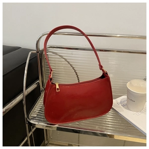 Red glossy faux leather shoulder bag displayed on a modern rack with fashion magazine