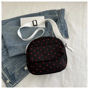 Flat lay of black nylon messenger bag with red heart prints and white strap