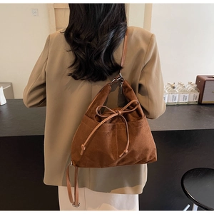 Detail einer braunen Wildleder-Schultertasche mit Schleife auf einem khakifarbenen Anzug