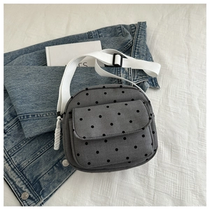 Close-up of gray nylon crossbody bag with black polka dots on denim fabric