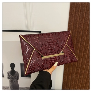 Close-up of burgundy envelope clutch with crocodile texture and gold metal trim detailing