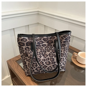 Dettaglio della borsa tote leopardata in tela con manici neri in pelle sul tavolo