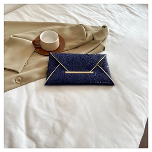 Detail of navy blue envelope clutch bag with snakeskin texture and gold metal V-trim