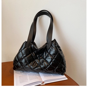 Detail of glossy black quilted down tote bag with classic diamond stitch on wood desk