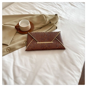 Detail of brown snake-pattern envelope clutch bag with elegant gold metal trim design