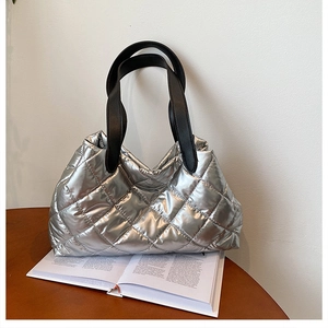 Detail of silver quilted tote bag with puffer texture and black leather shoulder straps