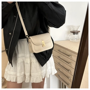 Chic beige crossbody square bag with gold twist lock worn over a black leather jacket