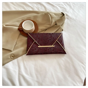Detail of burgundy snakeskin envelope clutch with gold metal trim and snap closure