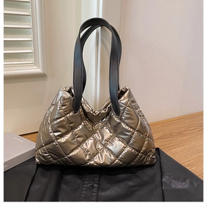 Detail of metallic quilted tote bag featuring gold fabric texture and black handles