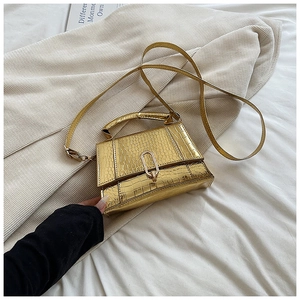 Détail d'un mini sac à main doré texture crocodile posé sur un costume beige élégant